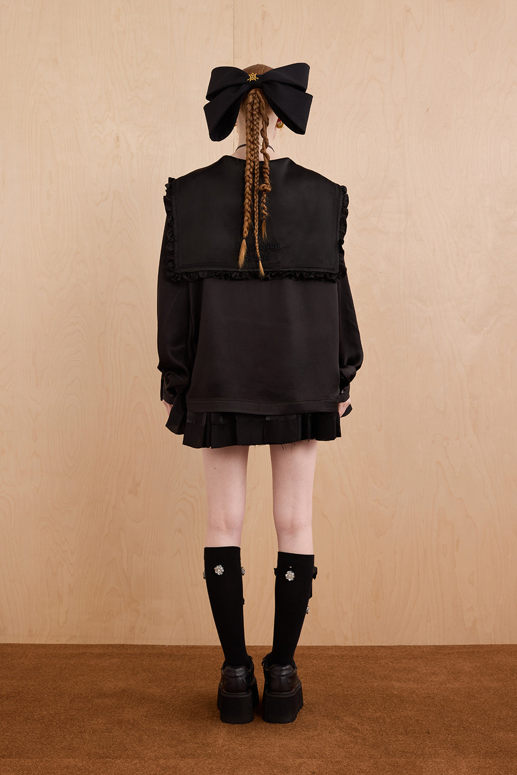 Person wearing a black outfit with a large bow on a beige background