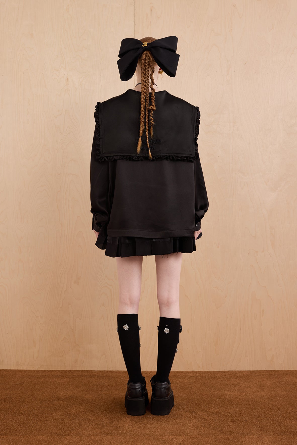 Person wearing a black outfit with a large bow on a beige background