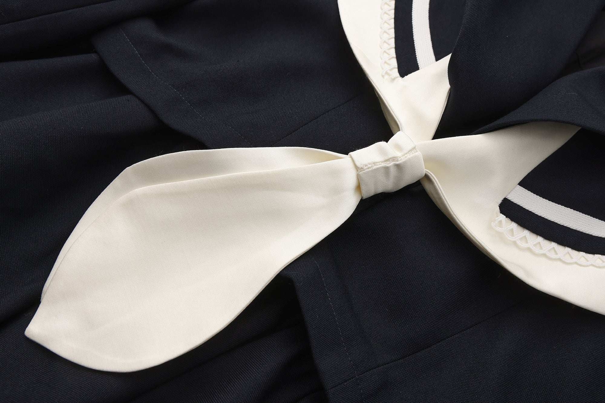 Close-up of pleated hem and patchwork panel details on navy jacket