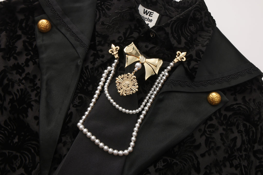 Close-up of sculptural bow tie clip, pearl chain, and engraved emblem detail