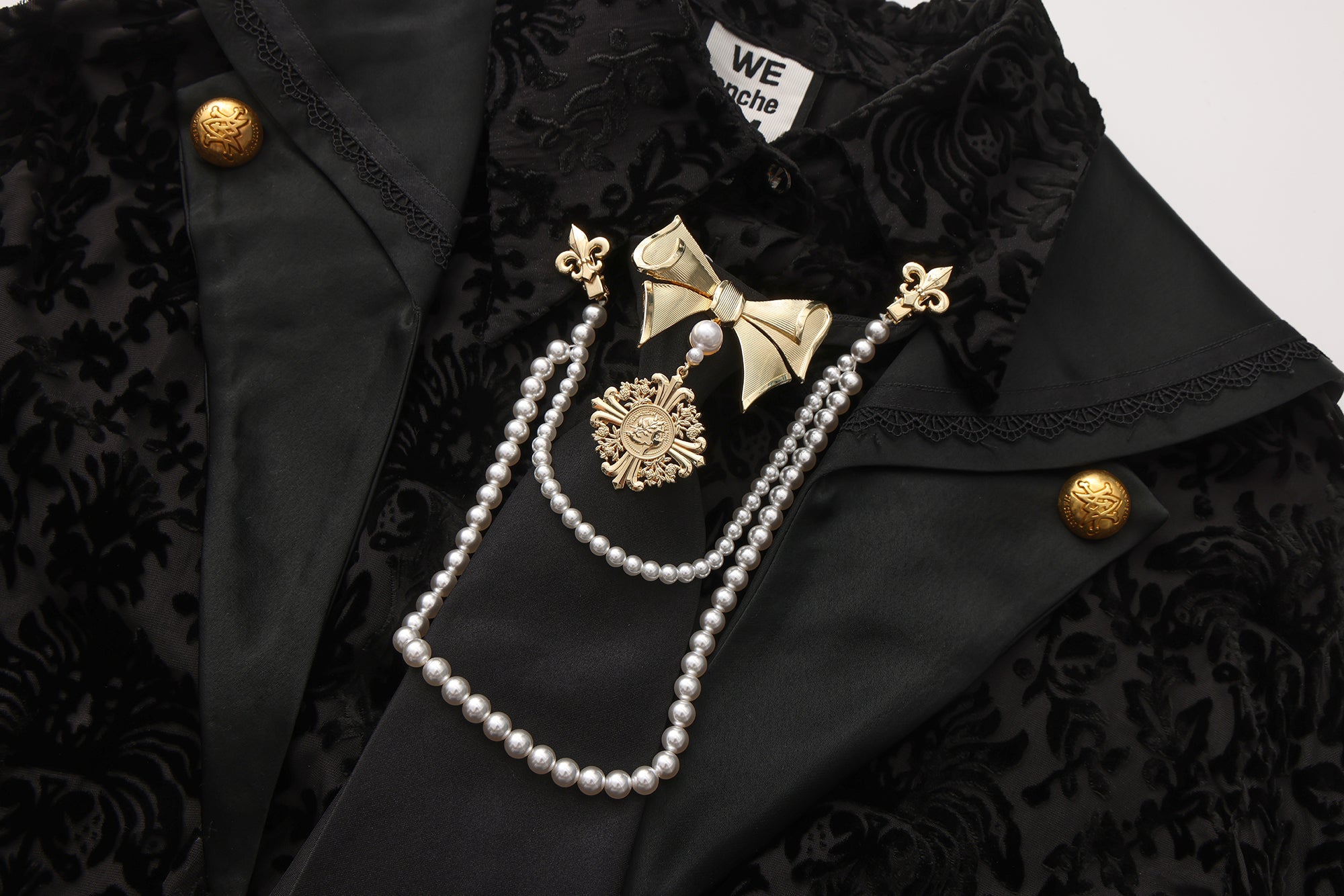 Close-up of sculptural bow tie clip, pearl chain, and engraved emblem detail