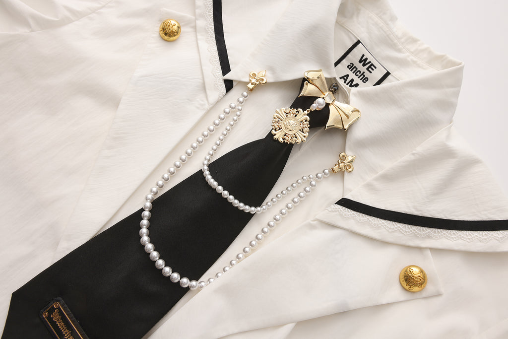 Close-up of sculptural bow tie clip, pearl chain, and engraved emblem detail