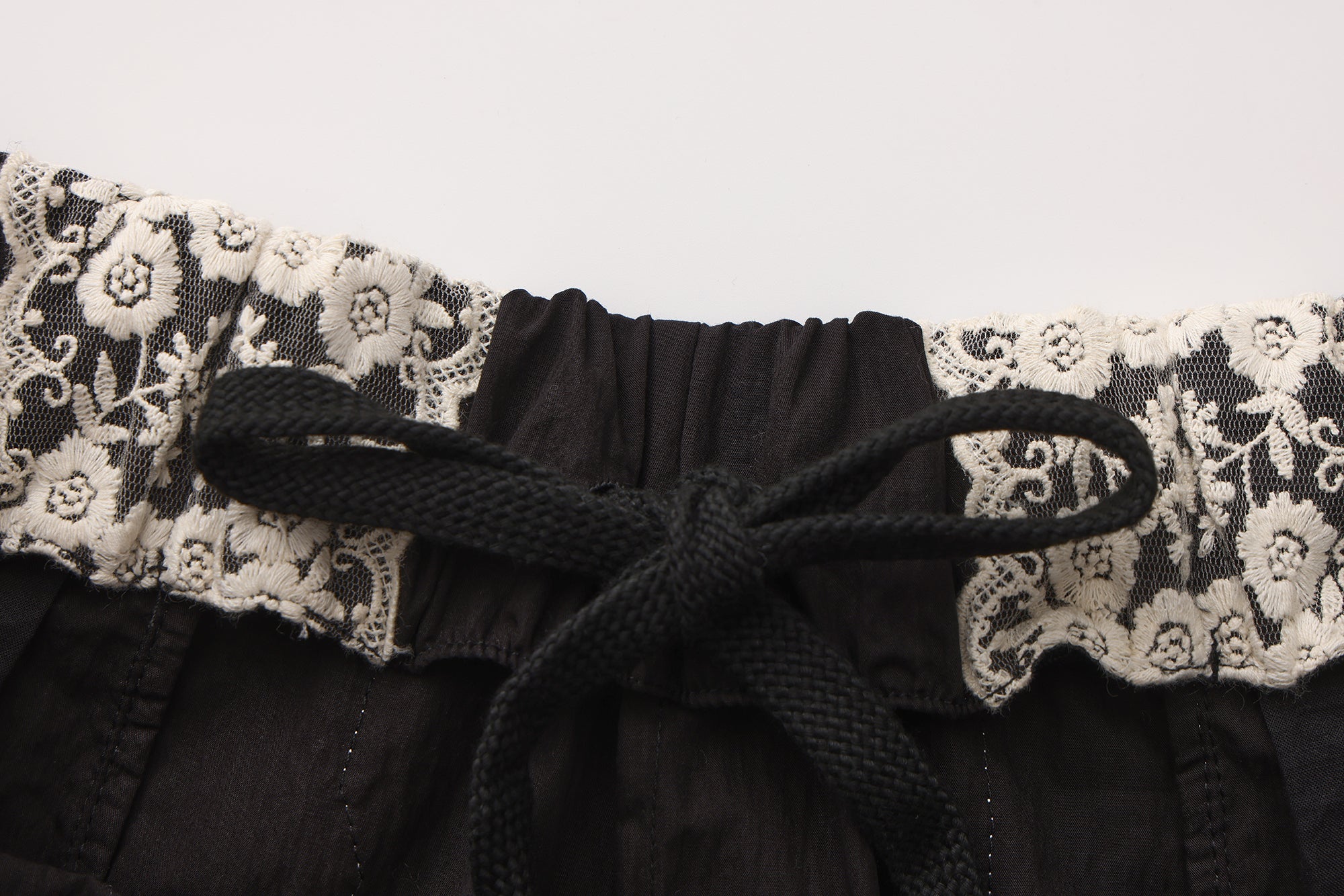 Close-up of embroidered lace patchwork and bow trim detail on trousers