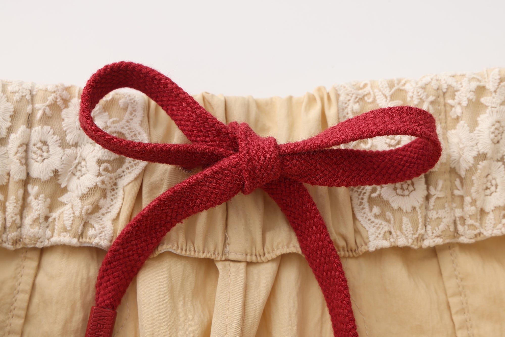 Close-up of embroidered lace patchwork and bow trim detail on trousers